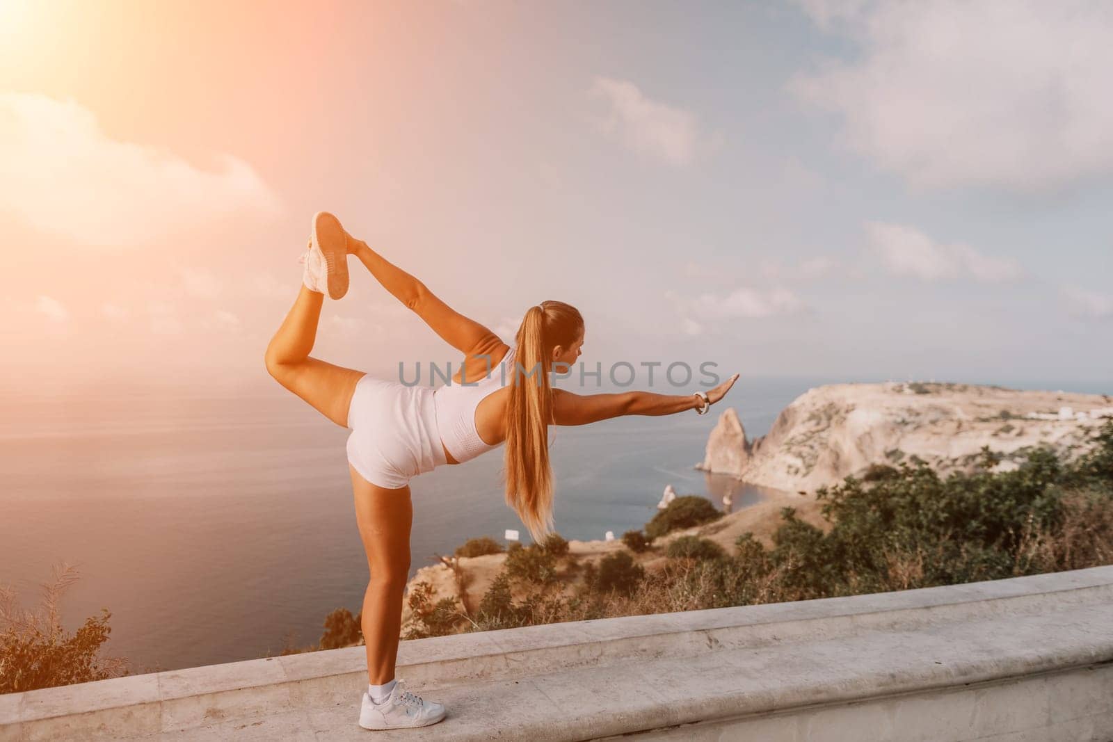 Fitness woman sea. A happy middle aged woman in white sportswear exercises morning outdoors in a park with a beach view. Female fitness pilates yoga routine concept. Healthy lifestyle. by panophotograph