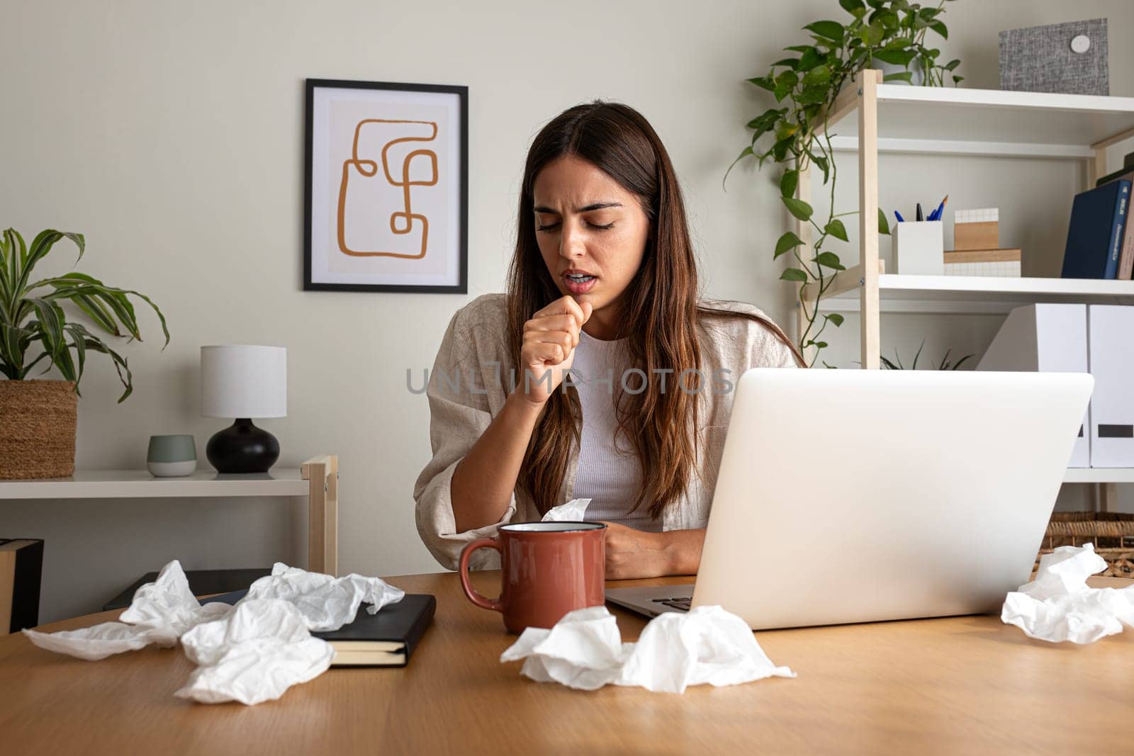 Sick woman working from home office feeling sick, coughing. Woman with the flu while working with laptop. by Hoverstock