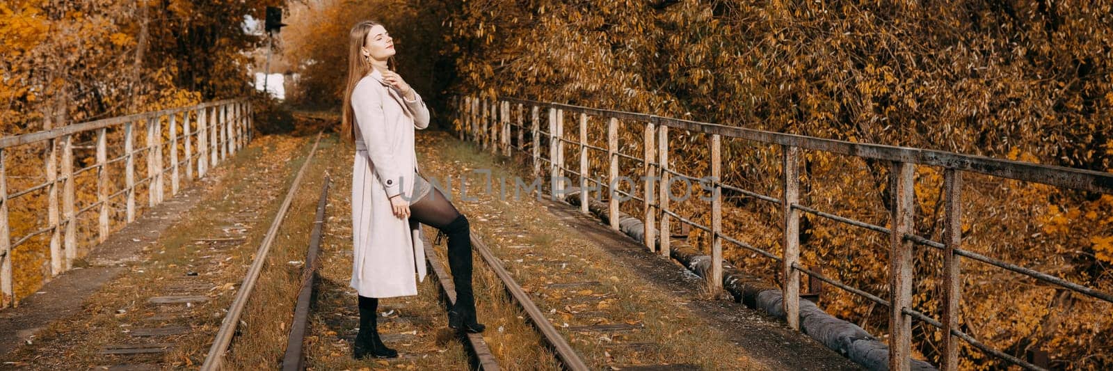 A beautiful long-haired woman walks through the autumn streets. Railway, autumn leaves, a woman in a light coat.