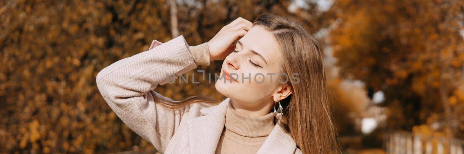 A beautiful long-haired woman walks through the autumn streets. Railway, autumn leaves, a woman in a light coat.