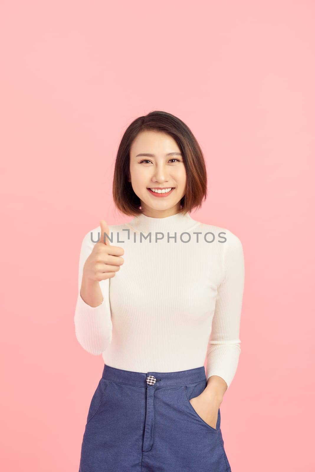 Young Asian woman show thumbs up on pink background by makidotvn