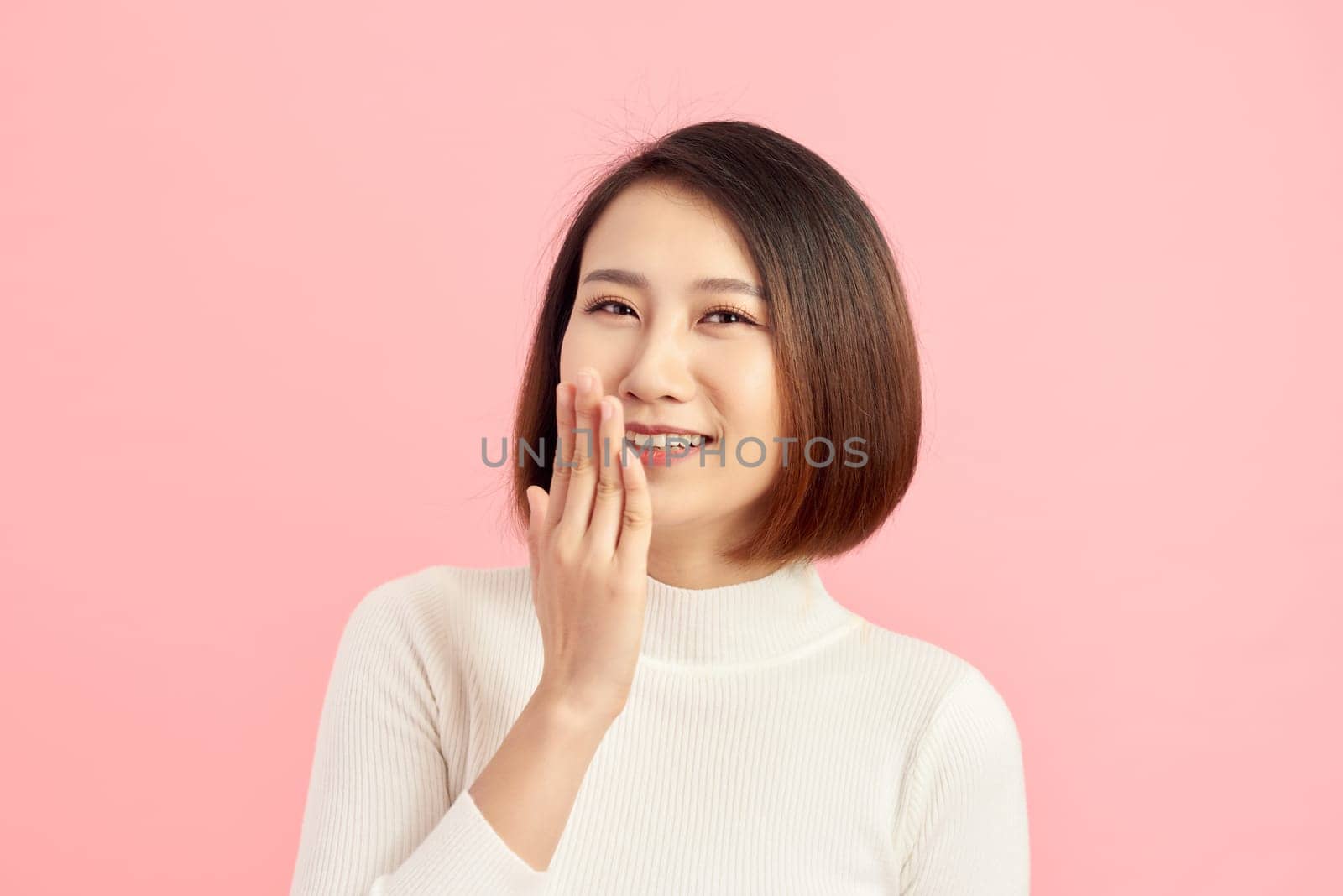 Beautiful Asian woman showing hand while smiling. Over pink background