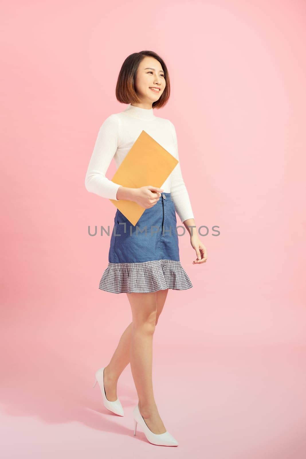 Full length portrait of a happy asian businesswoman holding document while walking isolated over pink background by makidotvn