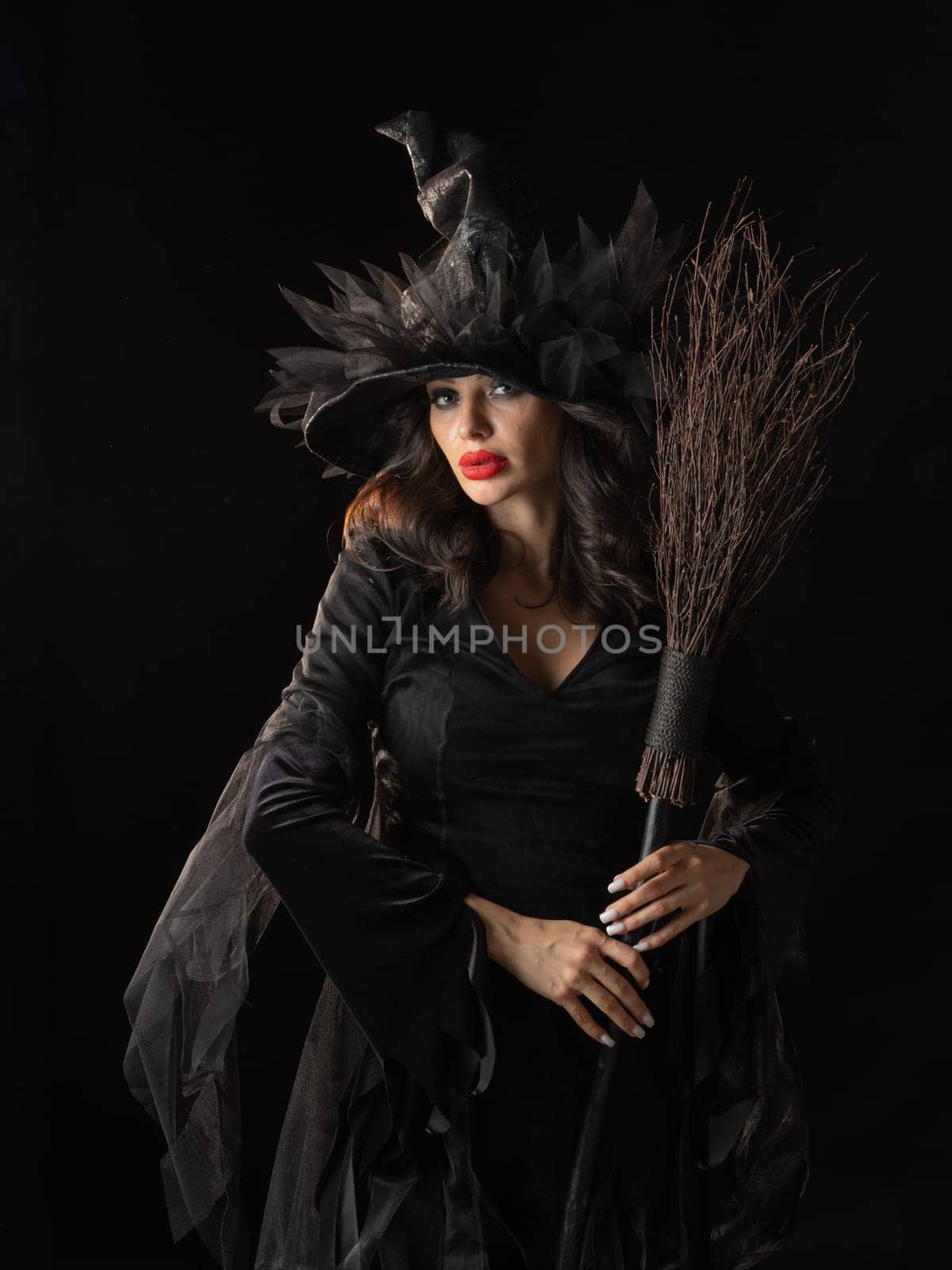 Charming halloween witch with broom over black background, woman beauty portrait, artistic make-up and costume