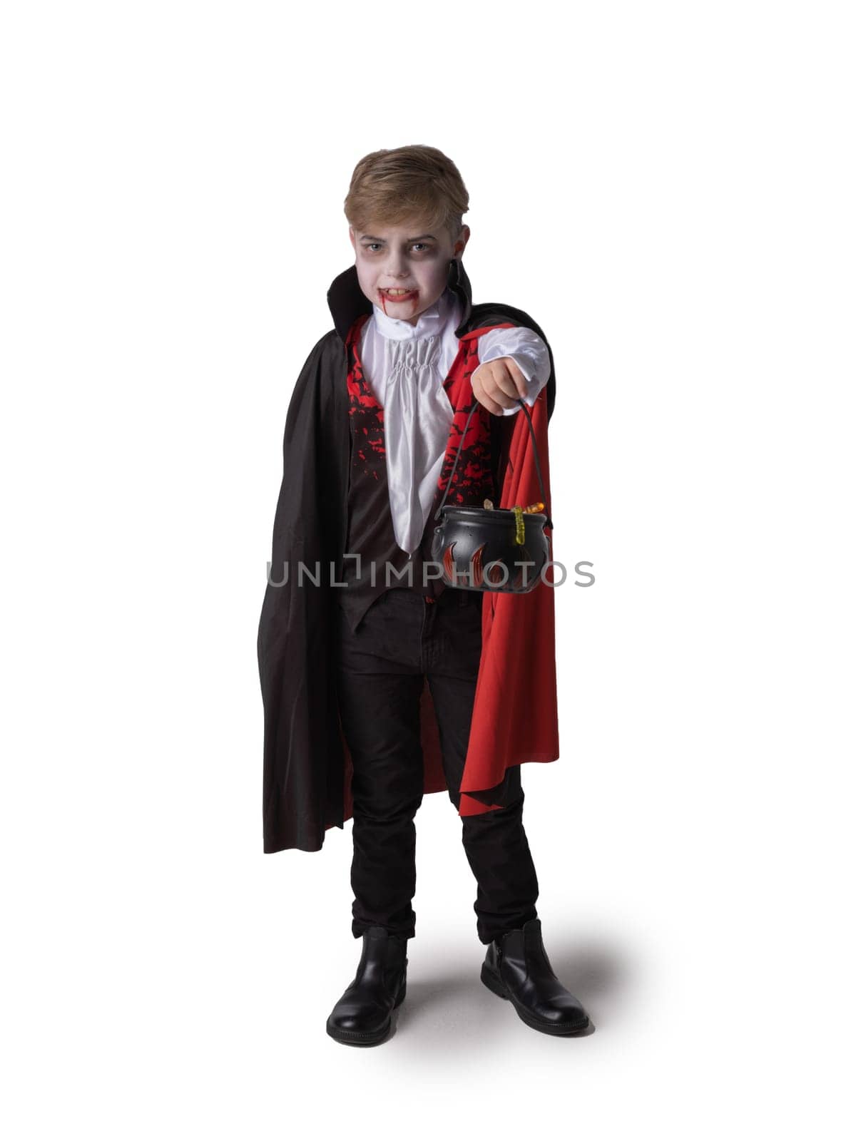 Boy in Halloween vampire makeup costume holding cauldron with sweets isolated on white background