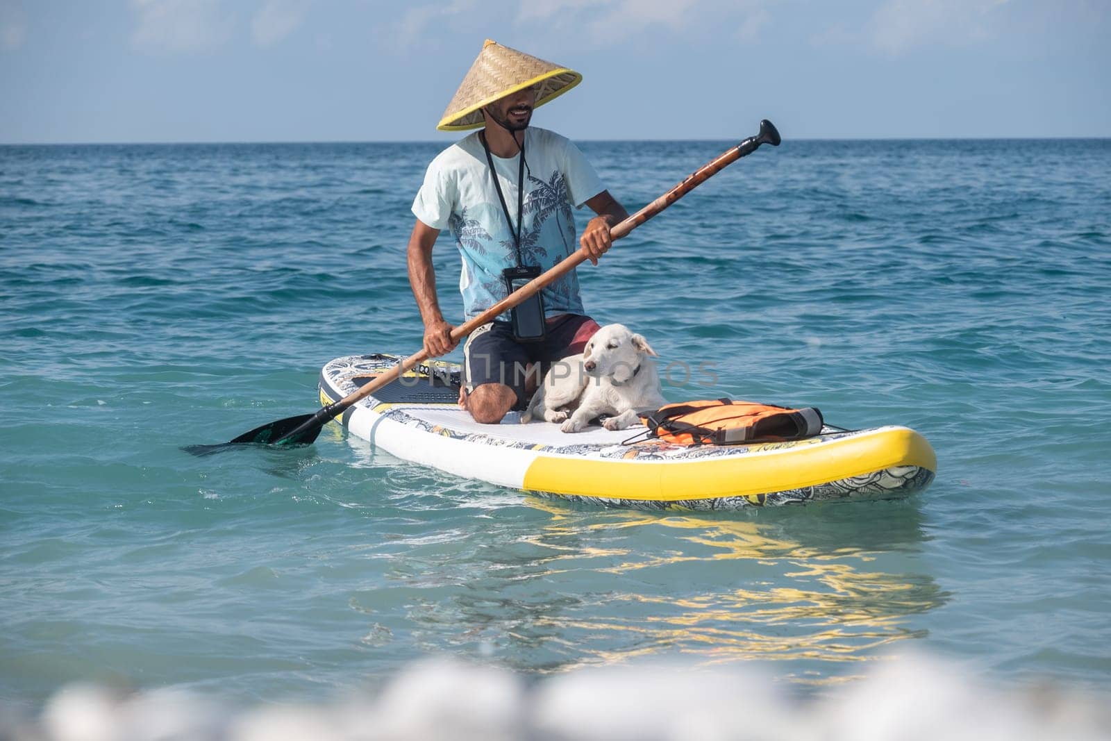 guy on a sup board with a paddle with a dog stands on the sea in summer