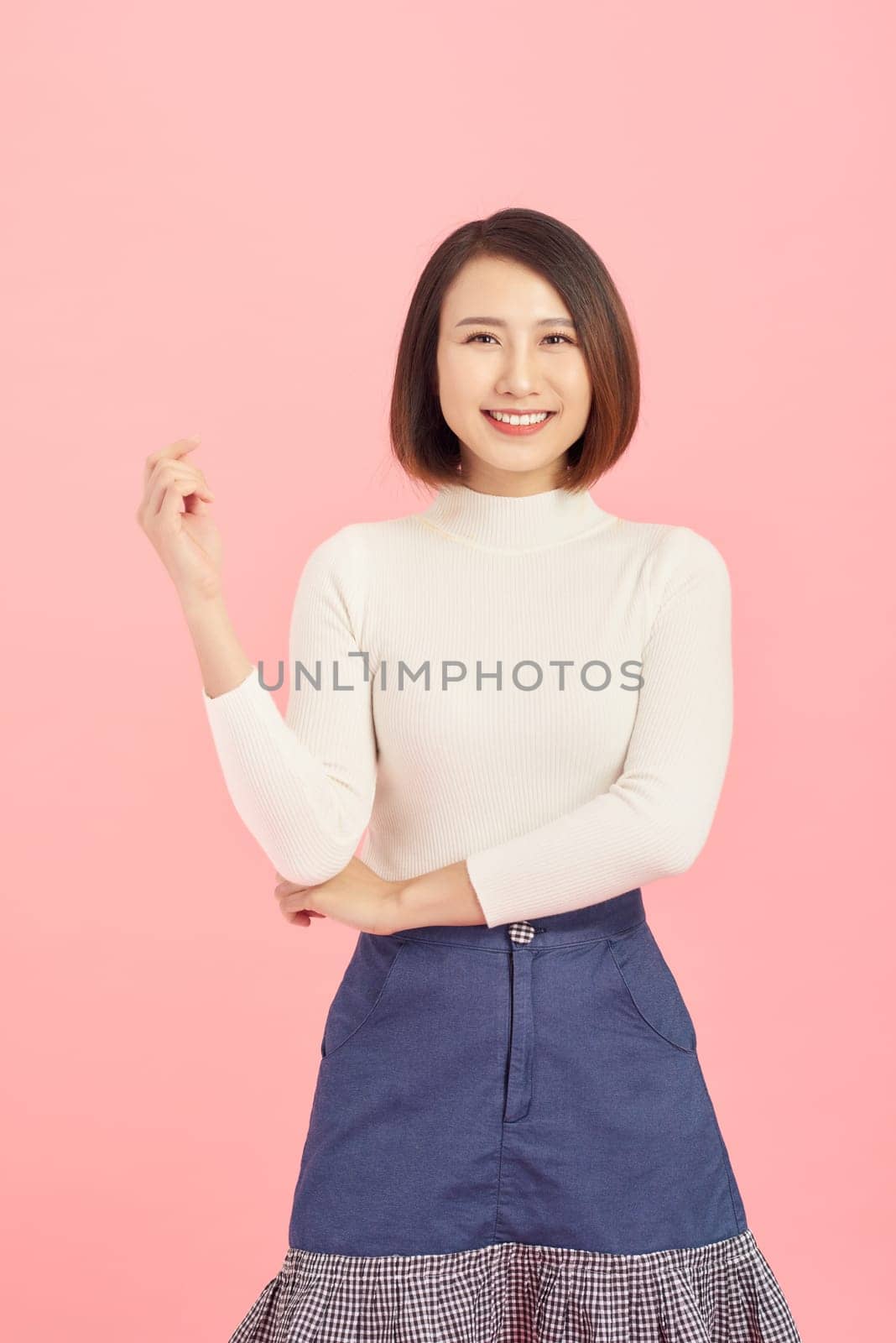 Cheerful young beautiful Asian woman showing her hand while standing over pink background. by makidotvn
