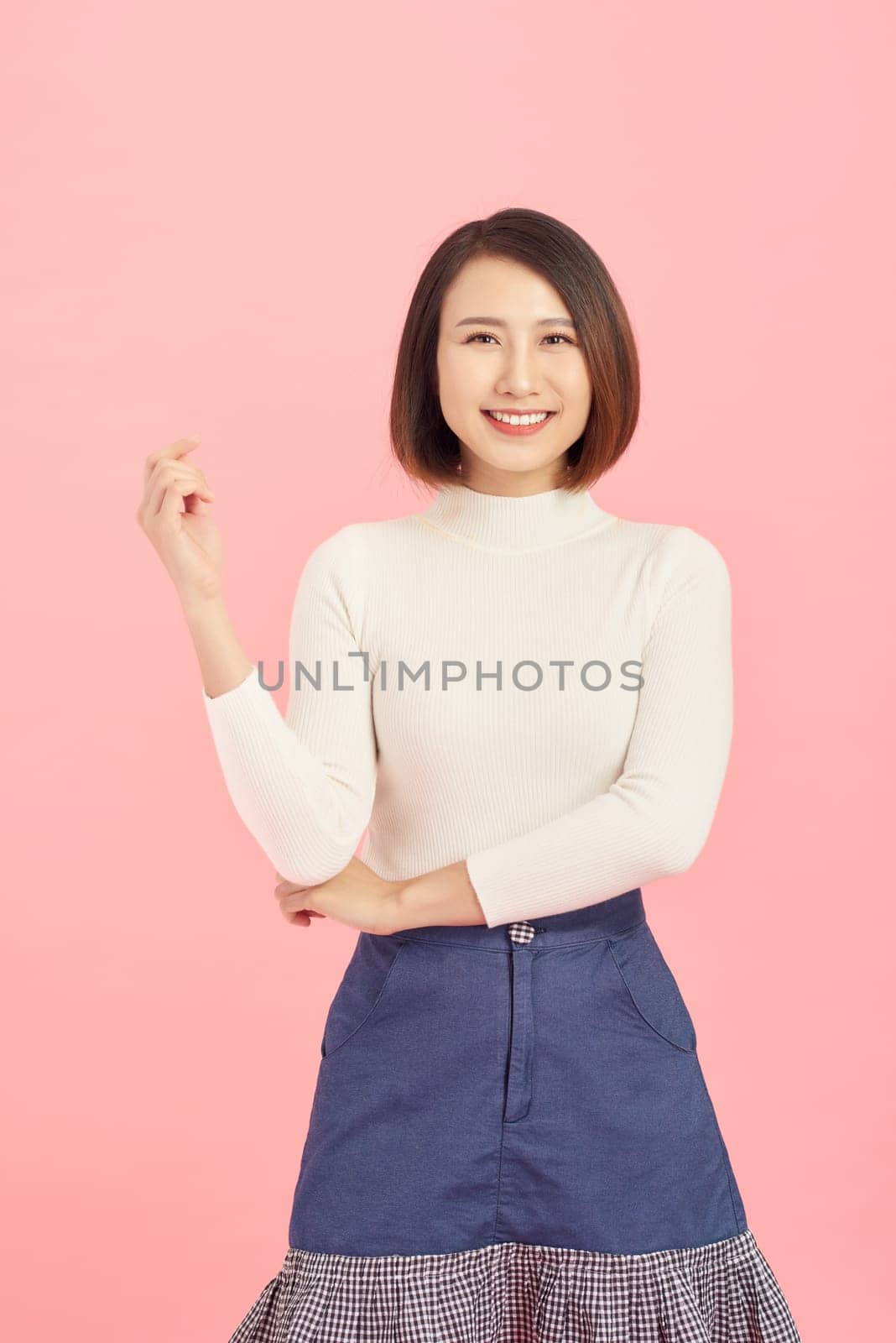 Cheerful young beautiful Asian woman showing her hand while standing over pink background.