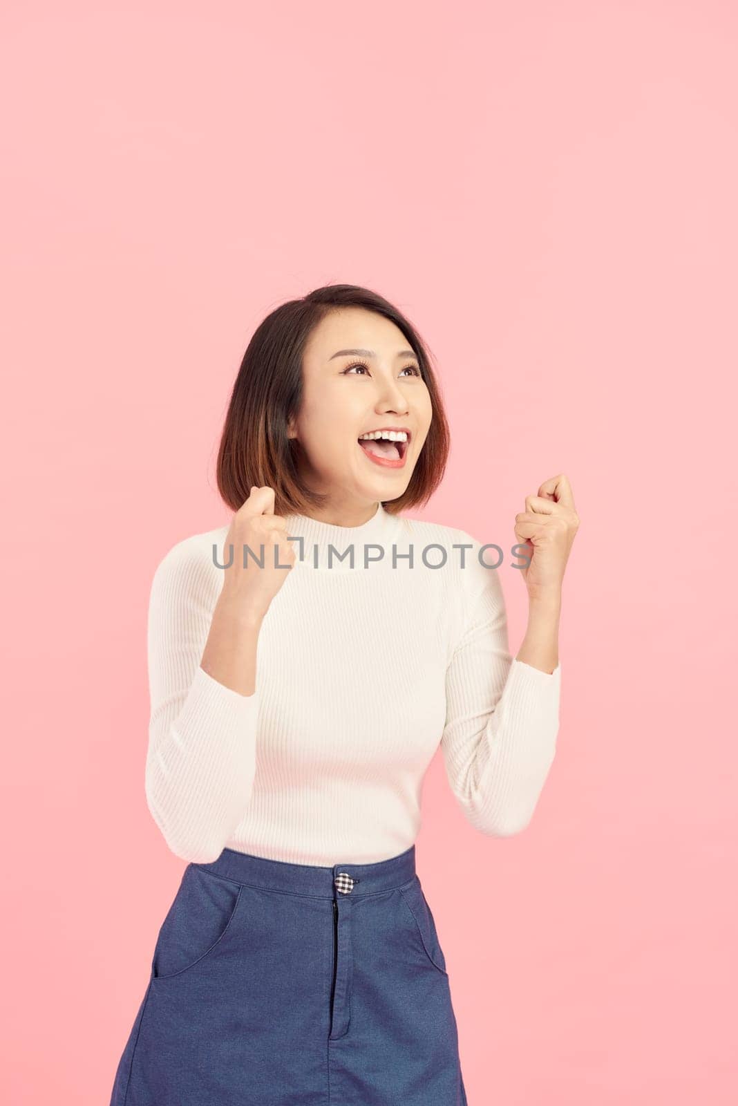 Portrait of an excited asian businesswoman looking at camera isolated over pink background by makidotvn