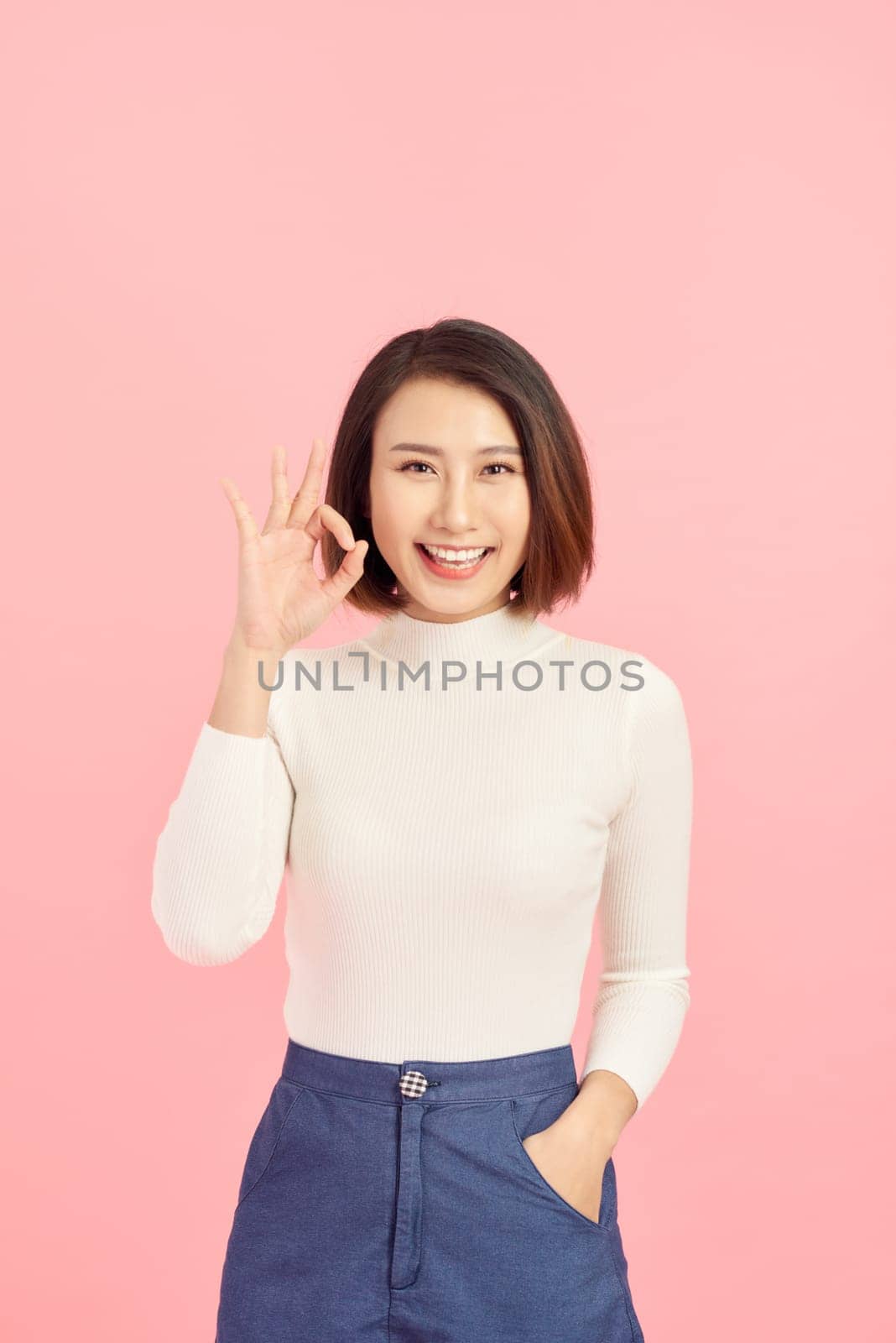 Portrait of young businesswoman showing ok sign while standing isolated on pink background.