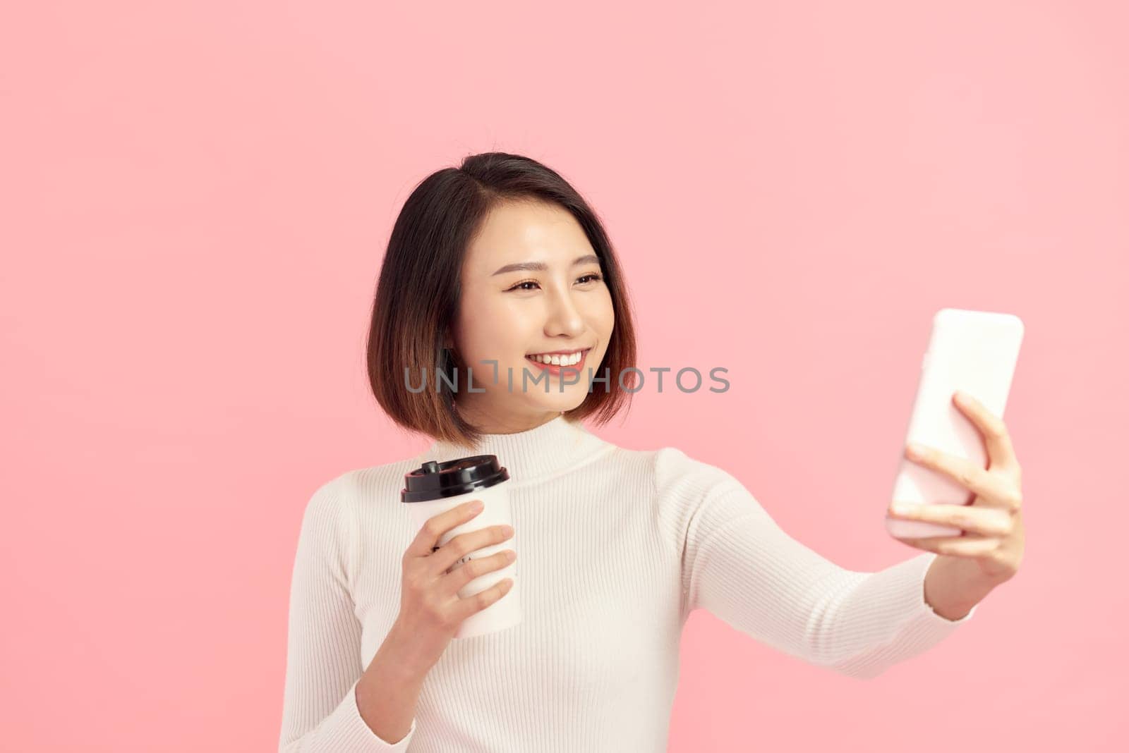 Young Asian woman selfie with her coffee cup on pink background. by makidotvn