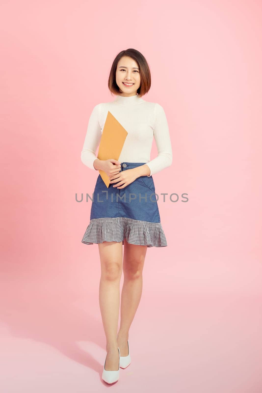 Full length portrait of a happy asian businesswoman holding document while walking isolated over pink background by makidotvn