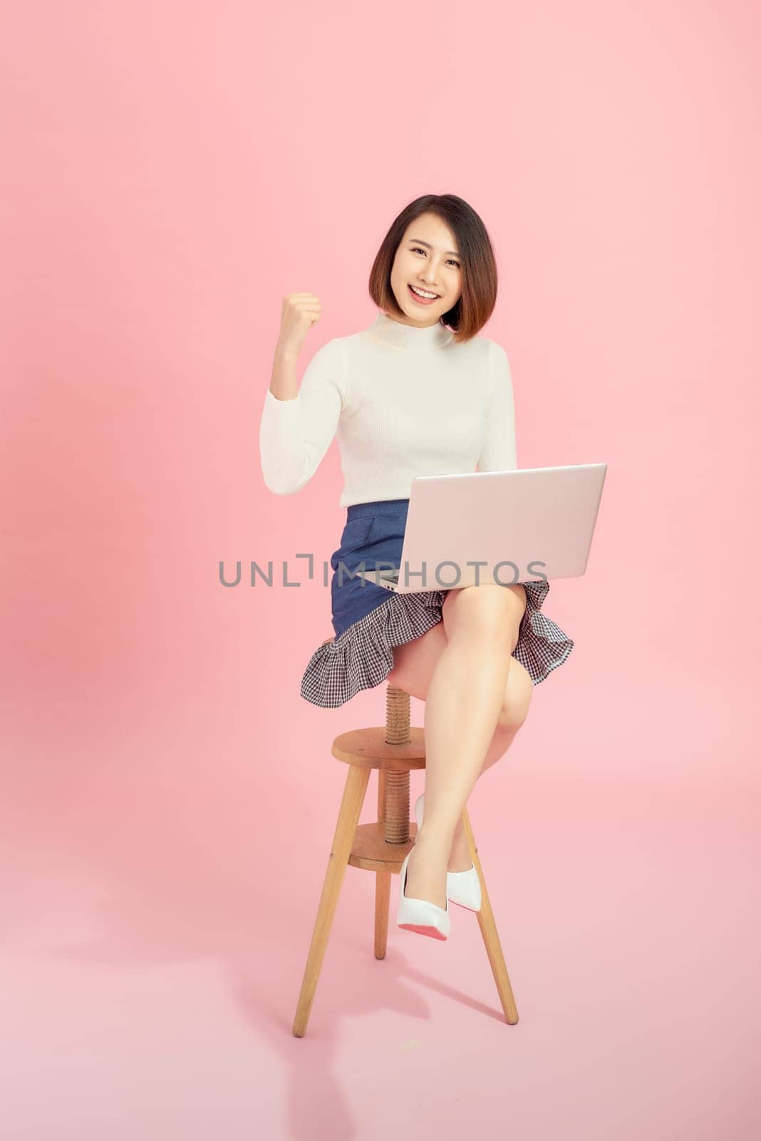 Young Asian woman using credit card to payment online with her laptop. Isolated on pink background. by makidotvn