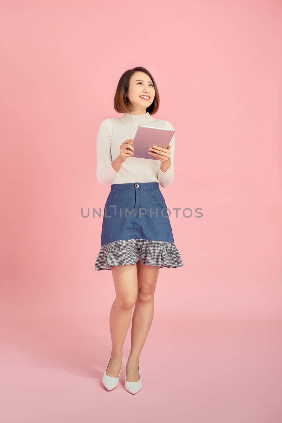 Young Asian woman reading book while standing over pink background. by makidotvn