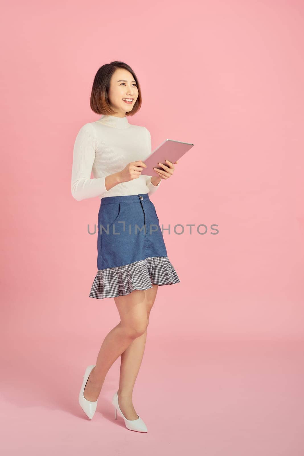Beautiful Asian woman hodling book and reading over pink background. Full length.