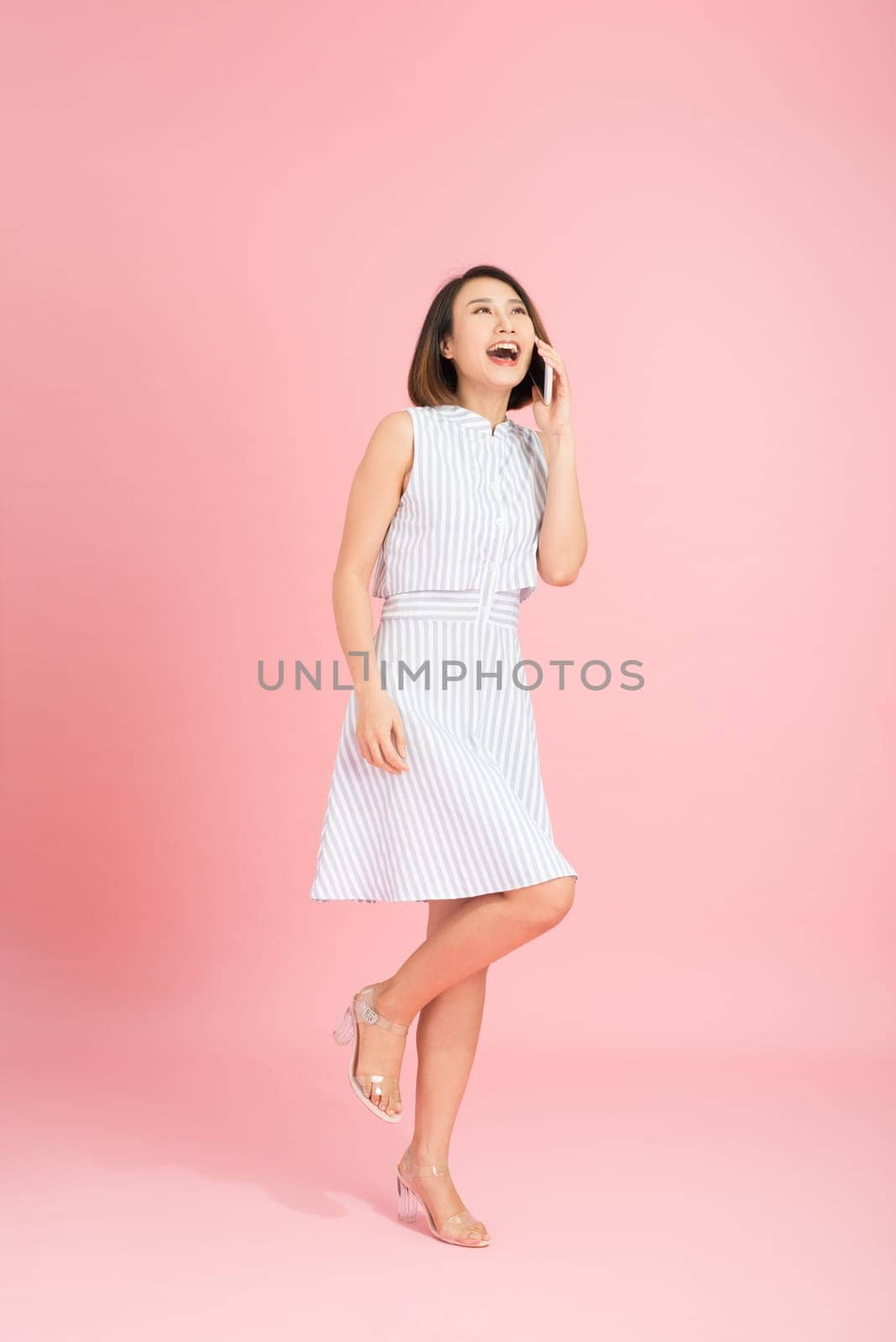 Full length portrait of a smiling casual girl using mobile phone isolated over pink background by makidotvn
