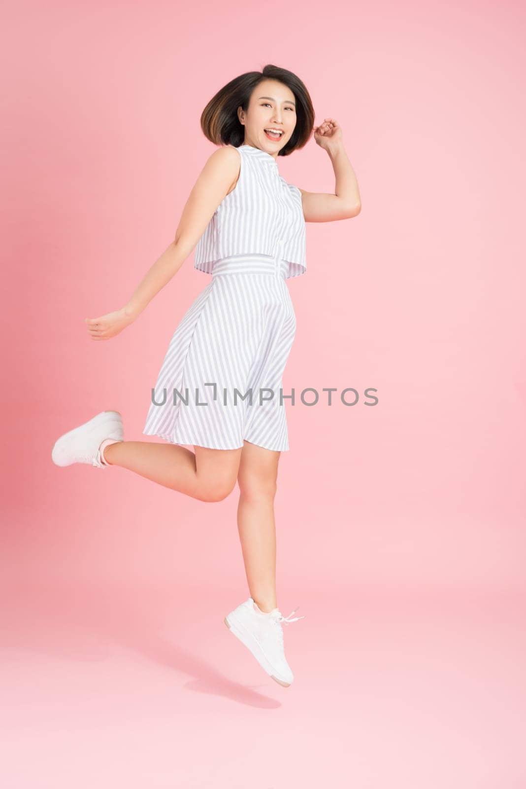 Freedom in moving. Surprised, pretty, happy young woman jumping and gesturing against pink studio background by makidotvn