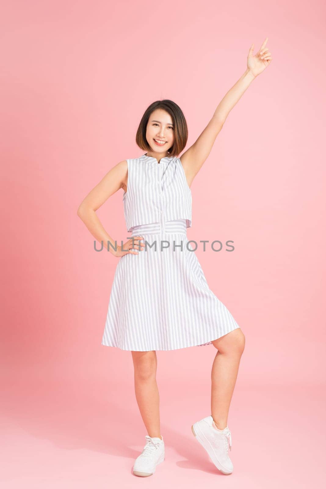 Beautiful young woman in light blue dress dancing on pink background