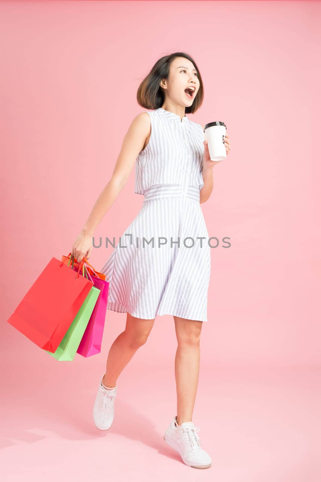 Woman carrying shopping bags enjoying cup of coffee concept isolated on pink with advertising area