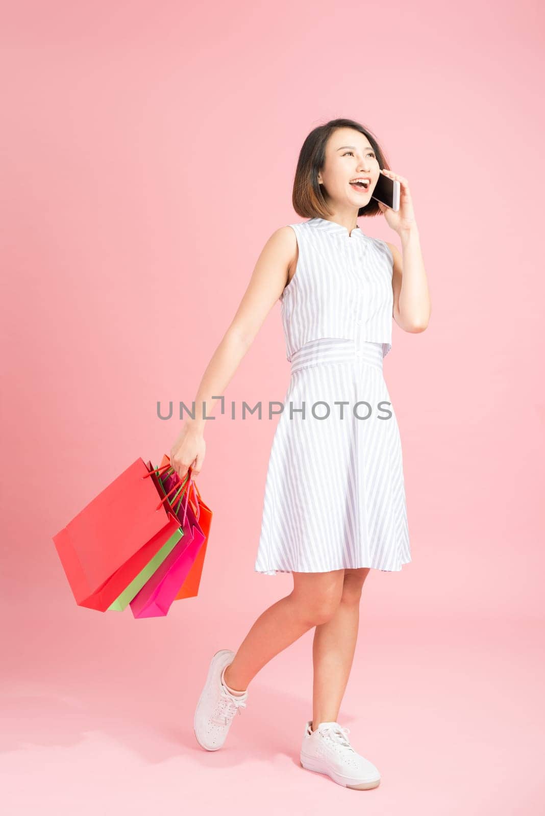 Woman carrying shopping bags and talking on mobile phone by makidotvn