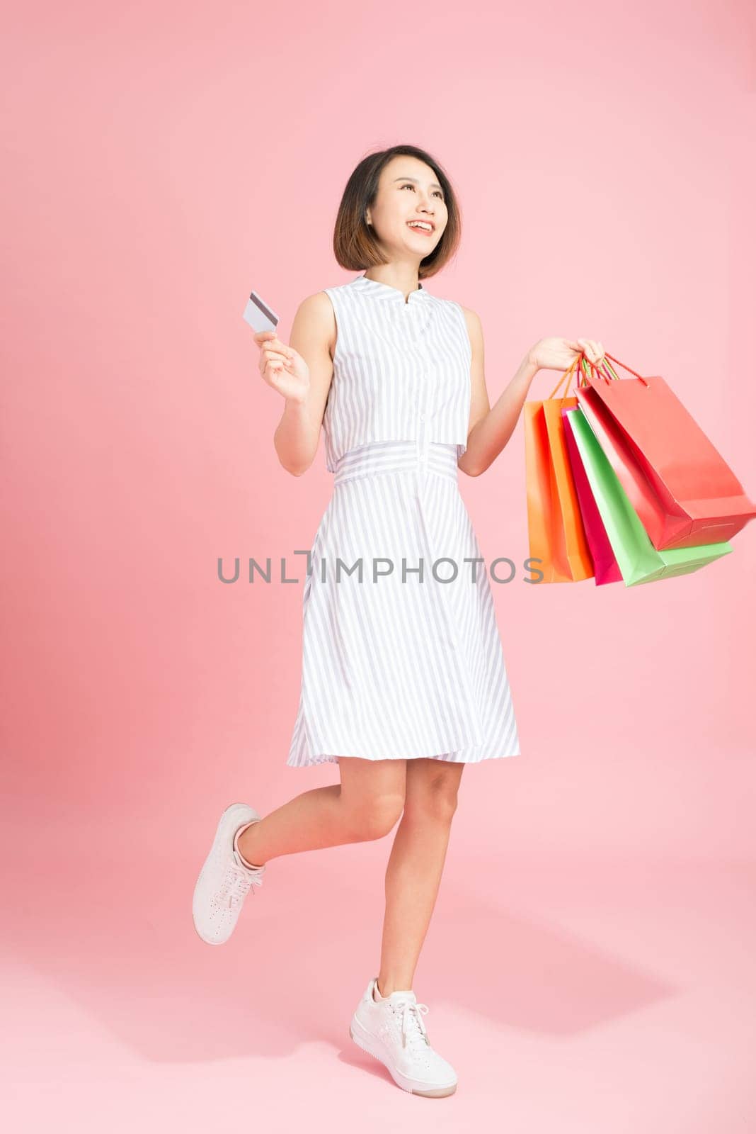 Portrait of a smiling pretty girl in dress with shopping bags holding credit card isolated over pink background