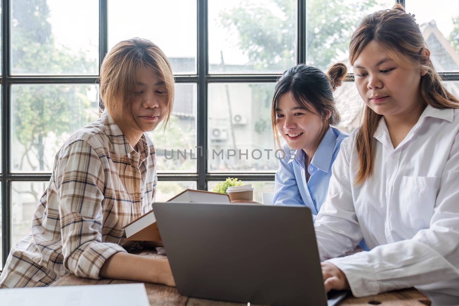 Asian College groups of students using laptop, tablet, studying together with notebooks documents paper for report near windows in classroom. Happy young study for school assignment, Soft focus by wichayada