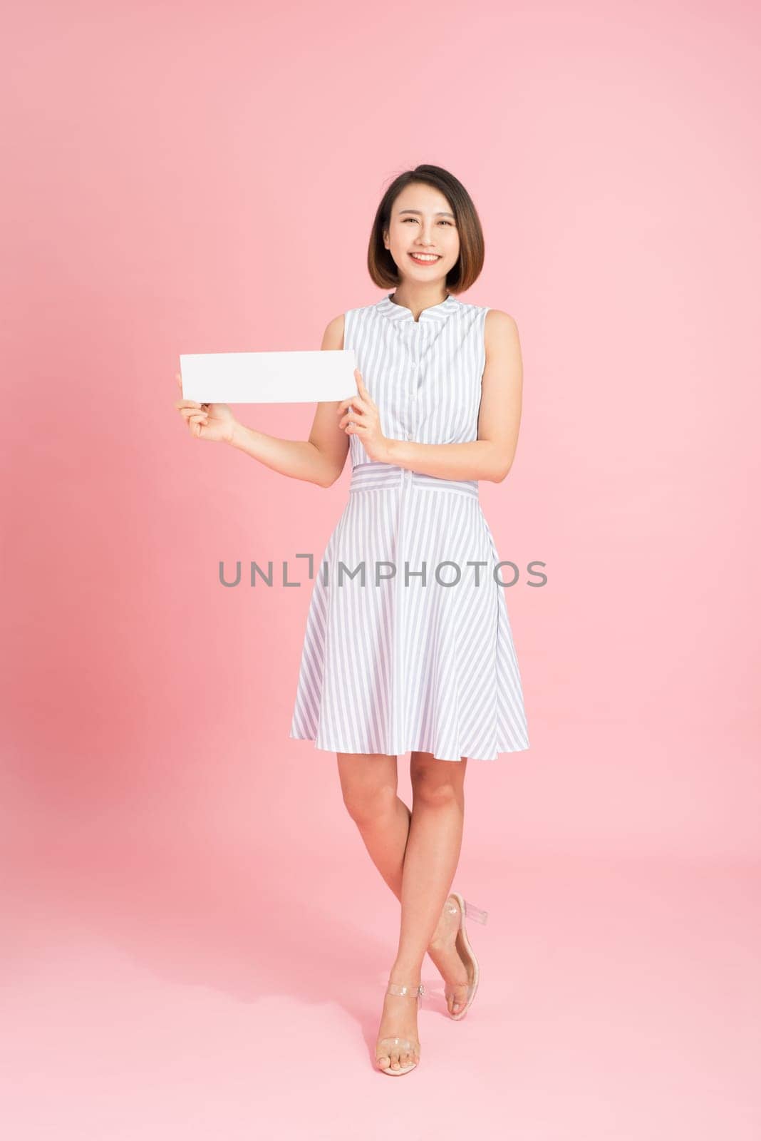 Your text here. Pretty young excited woman holding empty blank board. Studio portrait on white background. Mock up for design by makidotvn