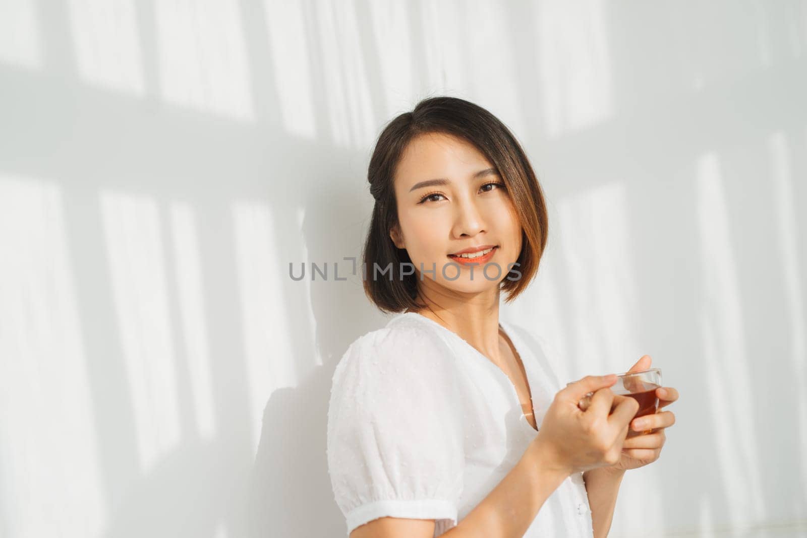 Beautiful woman standing by the window with a glass of hot tea in hand. Afternoon tea concept.