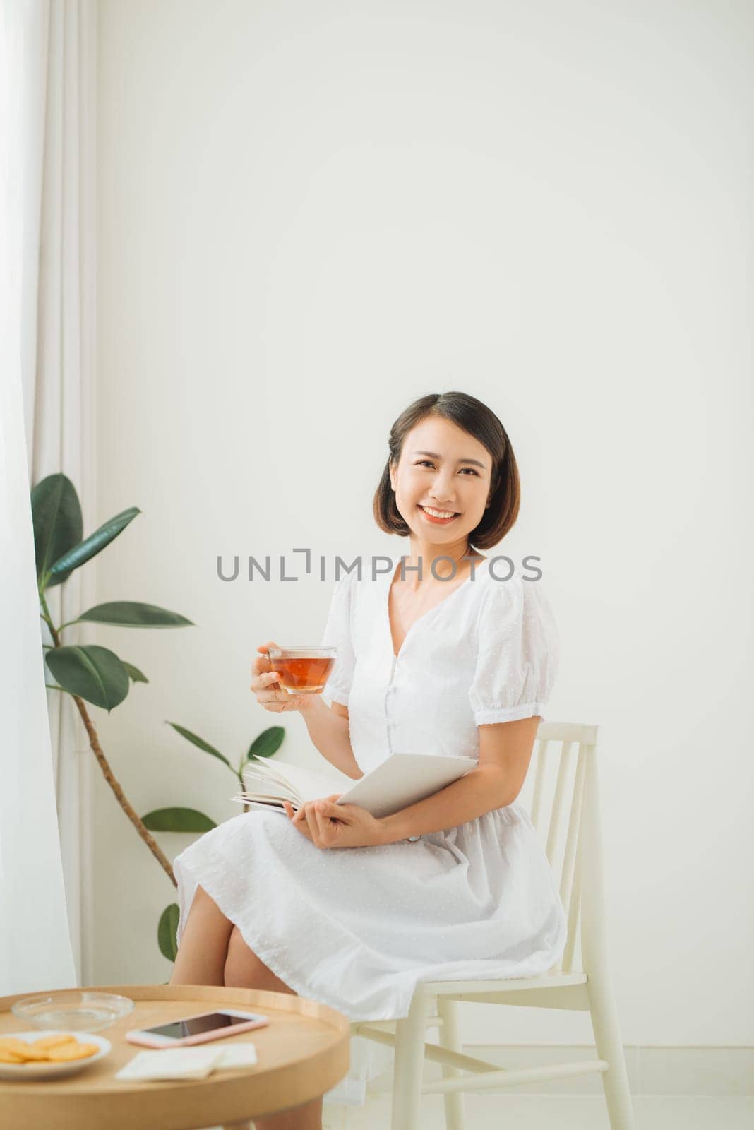 Young pretty woman sitting near window drinking tea and reading a book enjoys of rest