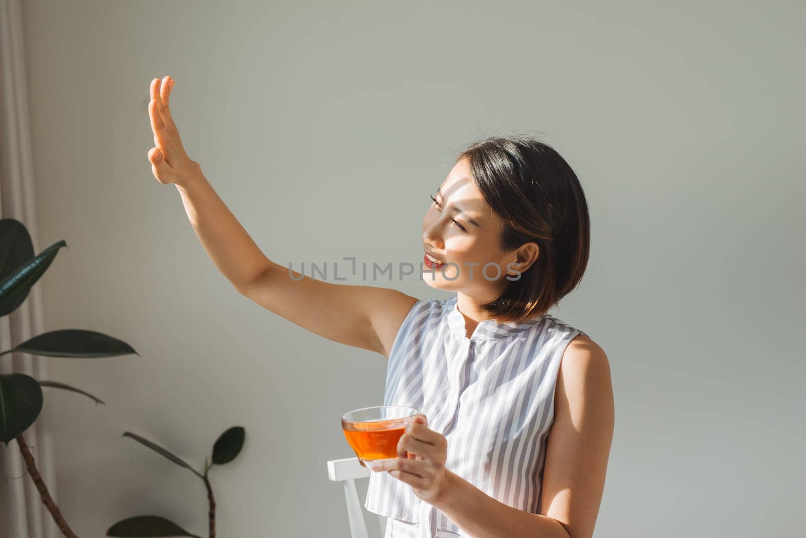 Portrait of a satisfied woman thinking looking at side holding a tea mug beside a window at home