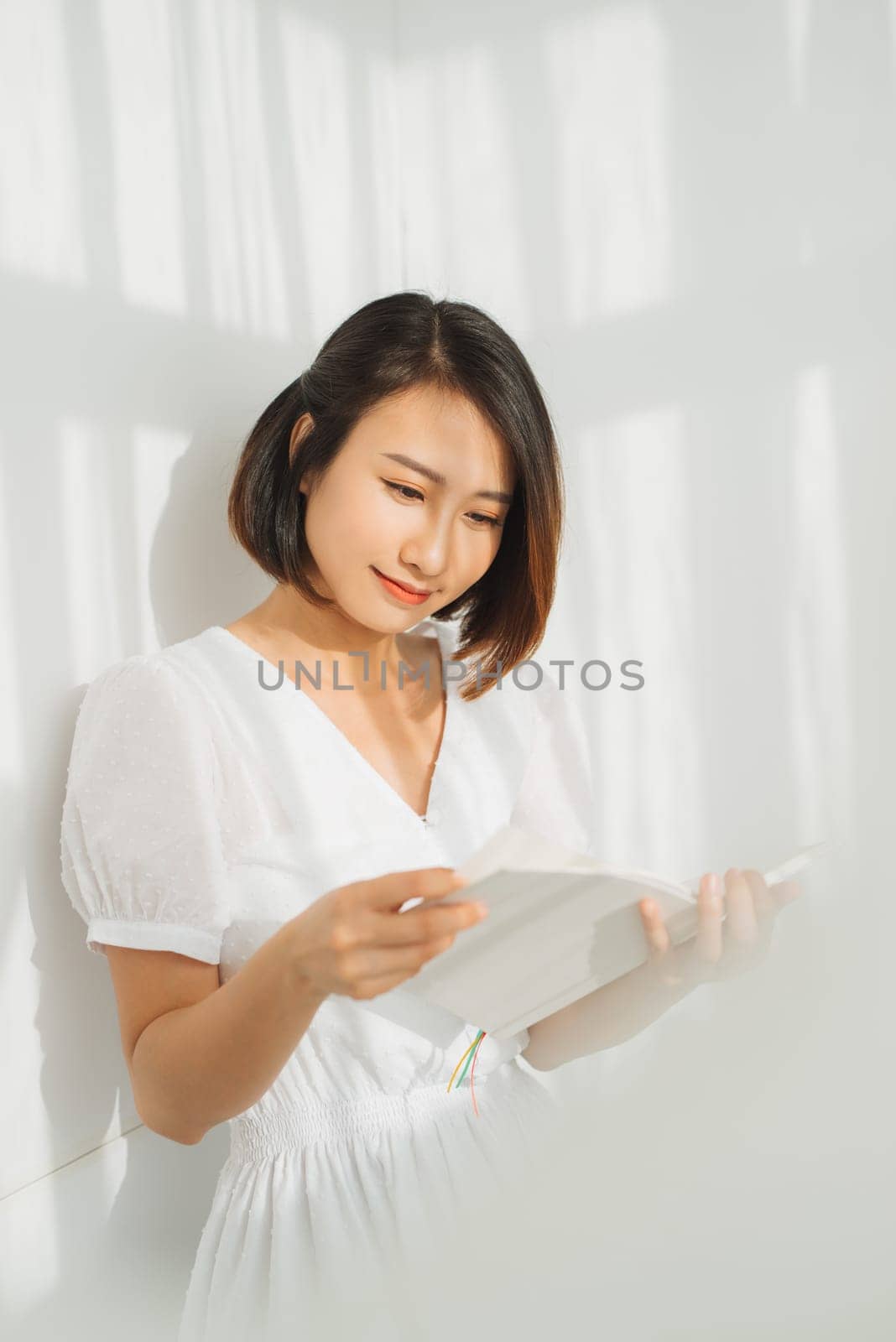 Portrait of beautiful asian woman relaxing by reading book near the window with sunlight of the morning by makidotvn