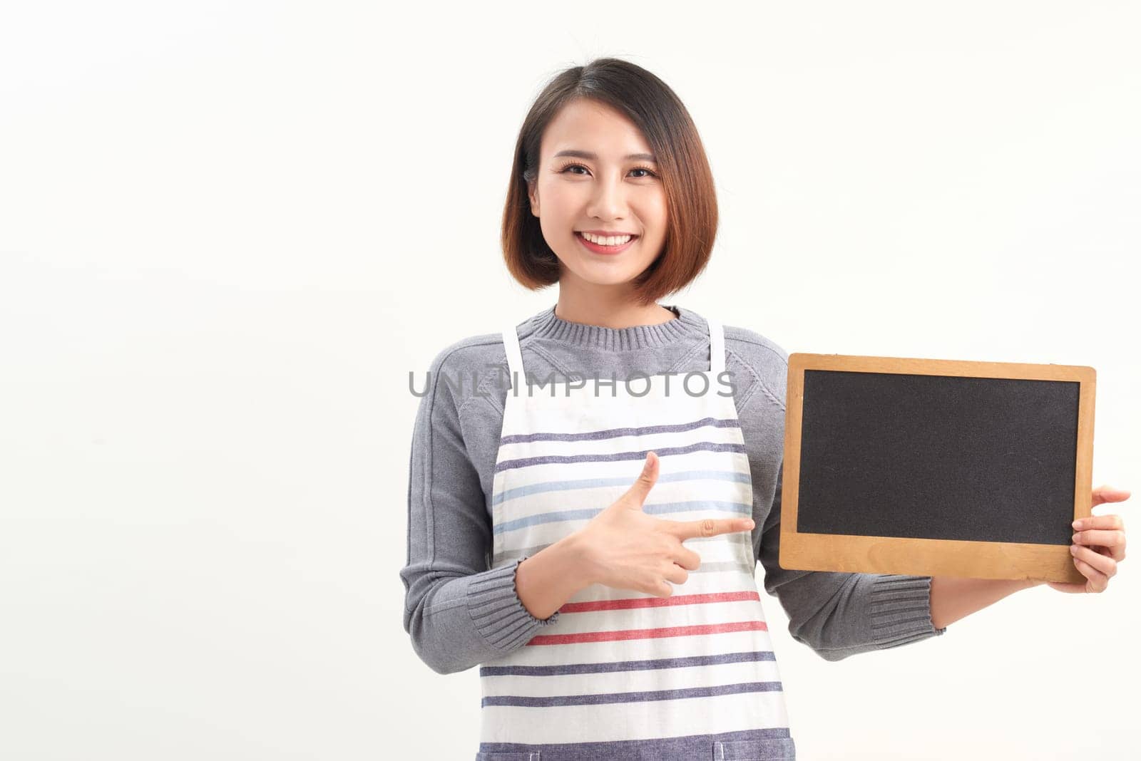 Asian female barista wear apron point at blank blackboard coffee menu at counter bar with smile face