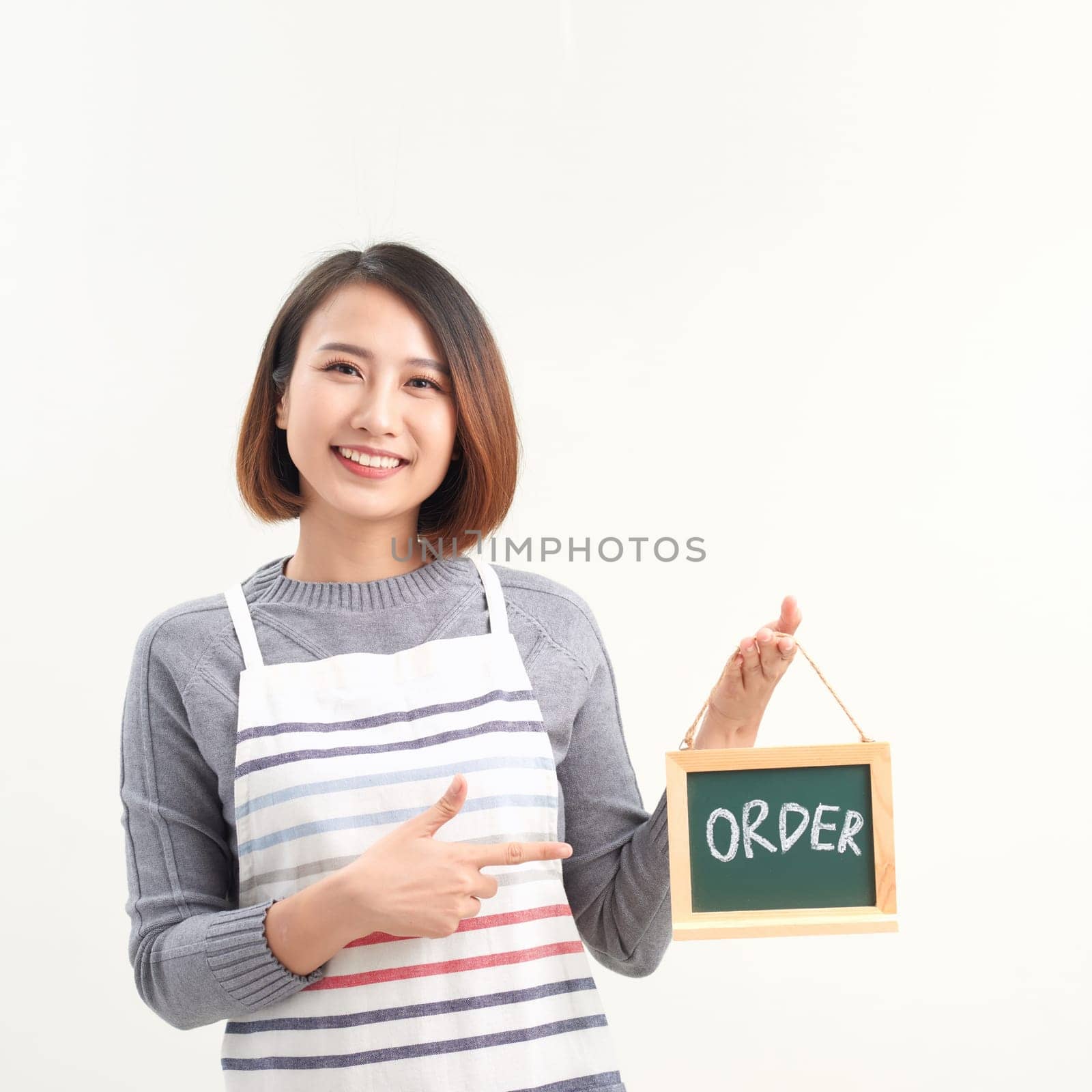 Cheerful girl holding advertising board with order word and pointing on it, white studio background