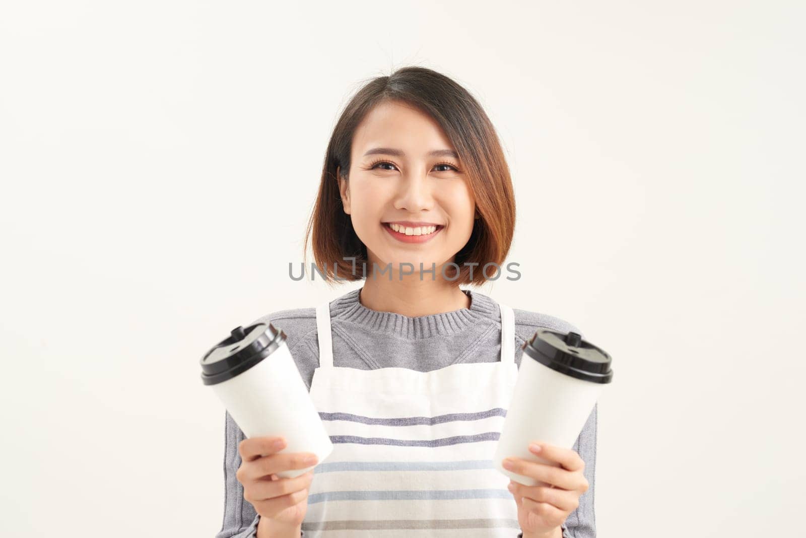 Portrait of kind friendly pleasant girl giving two big latte isolated on gray background copy-space