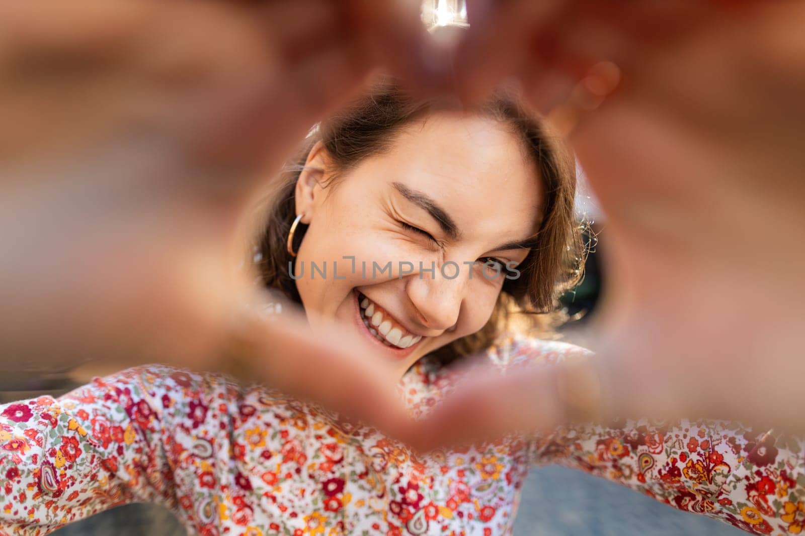 I love you. Portrait of Caucasian woman makes symbol of love, showing heart sign to camera, express romantic feelings, express sincere positive feelings. Charity, donation. Outdoors in city street