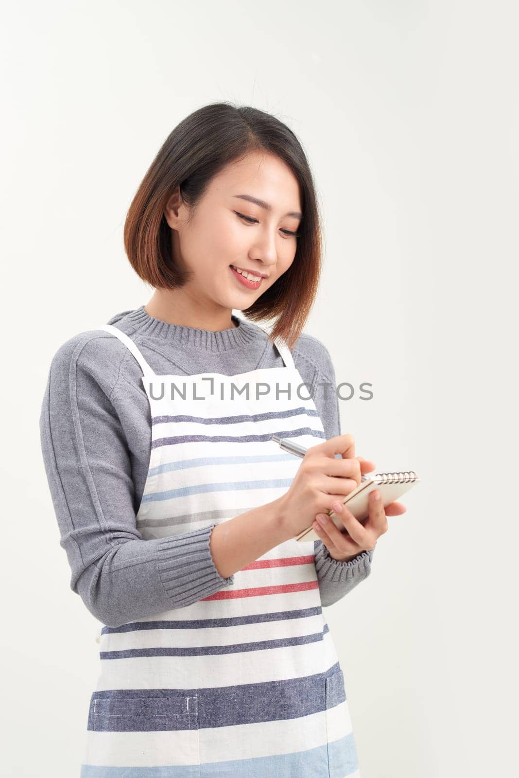 Head shot portrait of smiling waitress wearing black apron ready to take customer order, attractive woman with notebook and pen in hands looking at camera