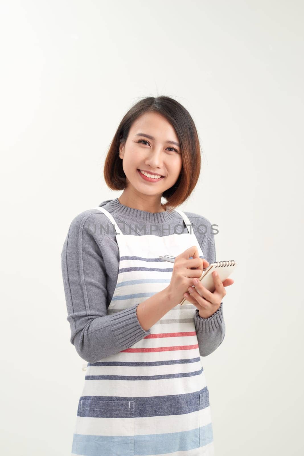 Happy attractive asian female waiter in apron writing order and looking at camera