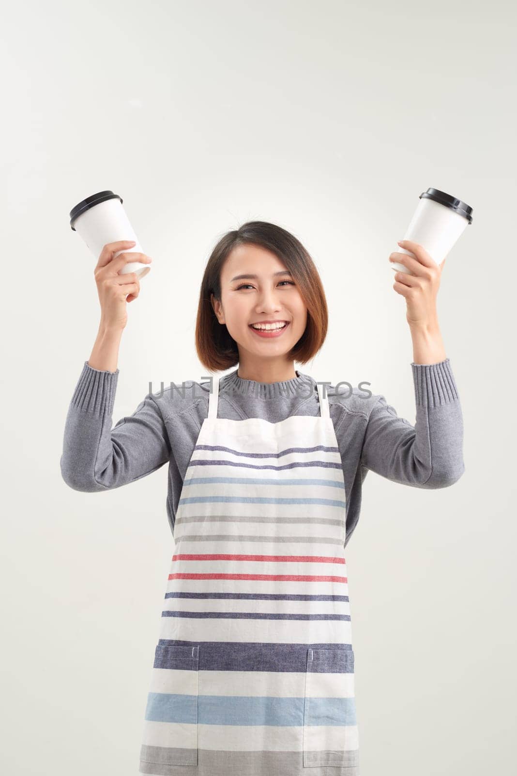 Charming girl holds disposable cup with drinks and looks directly to the camera isolated on white background