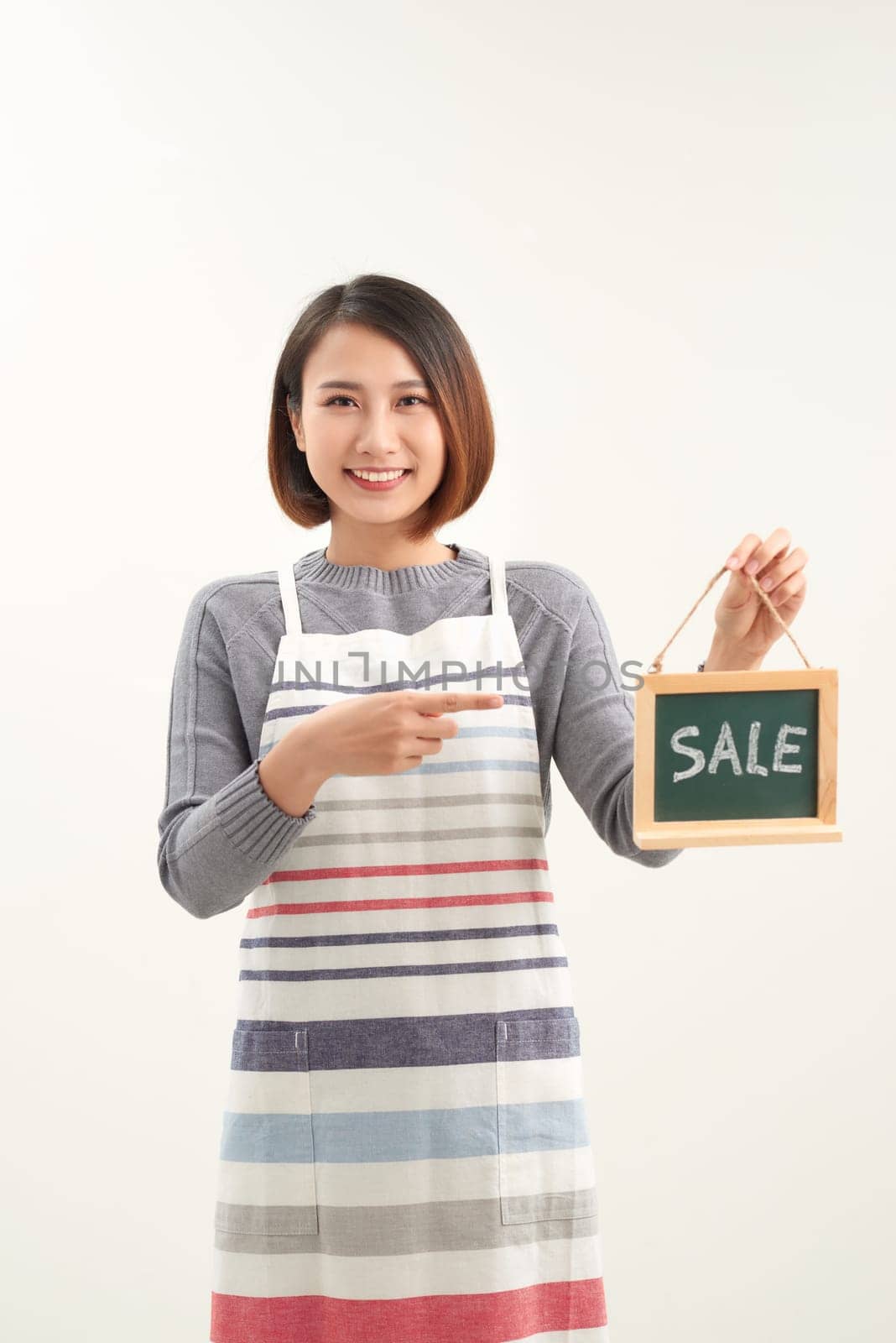 Cheerful girl holding  advertising board with sale word and pointing on it, white studio background by makidotvn