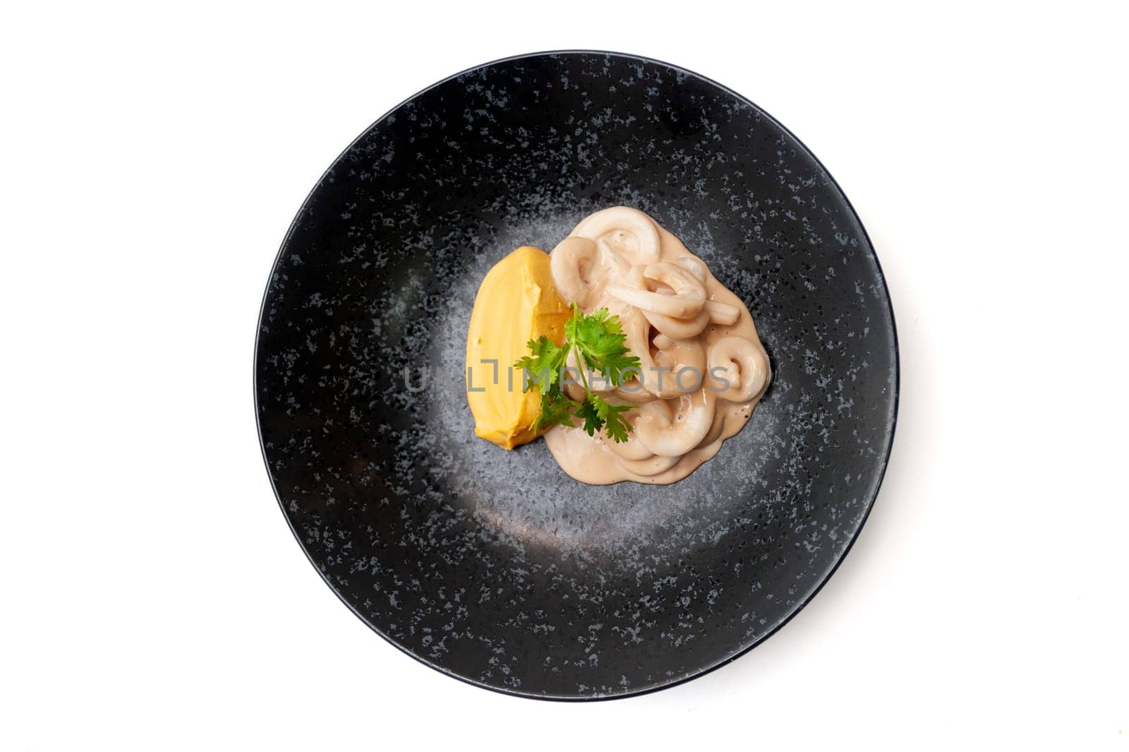 Squid rings in sauce with sweet potato puree on a black plate isolated. High quality photo
