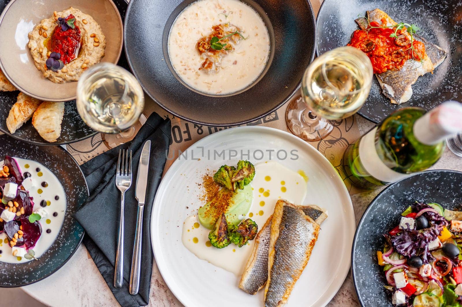 A set of Mediterranean cuisine dishes on a table in a restaurant with a glass and a bottle of white wine. View from above. High quality photo