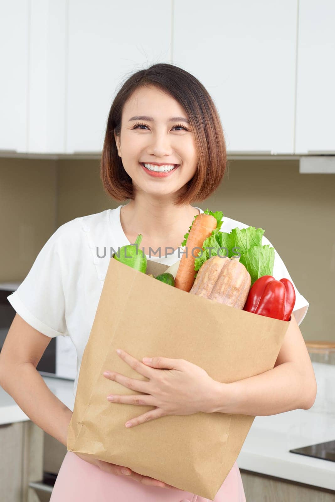 Young Asian woman holding grocery shopping bag with vegetables in the kitchen.