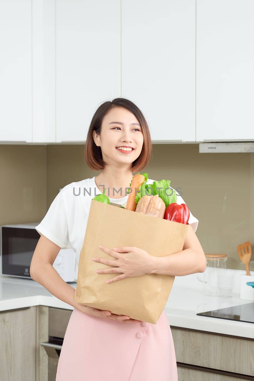 Portrait of happy young housewife with local market purchases in kitchen