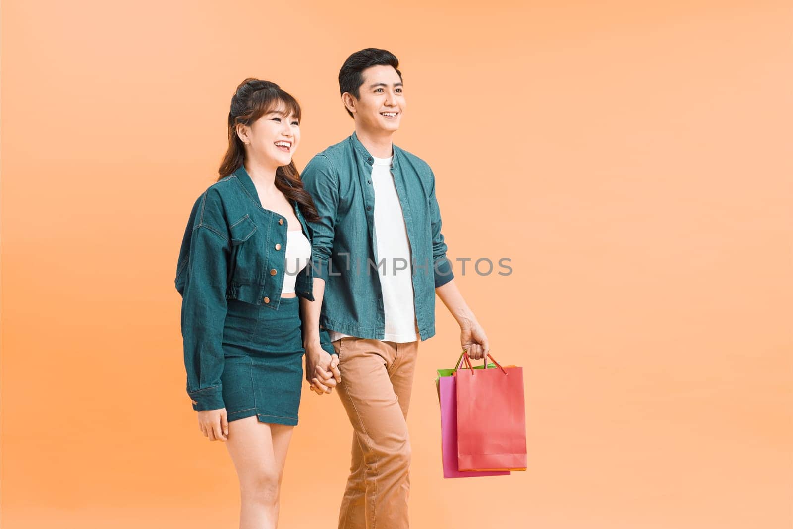 Happy asian couple holding shopping bags and smiling at camera isolated