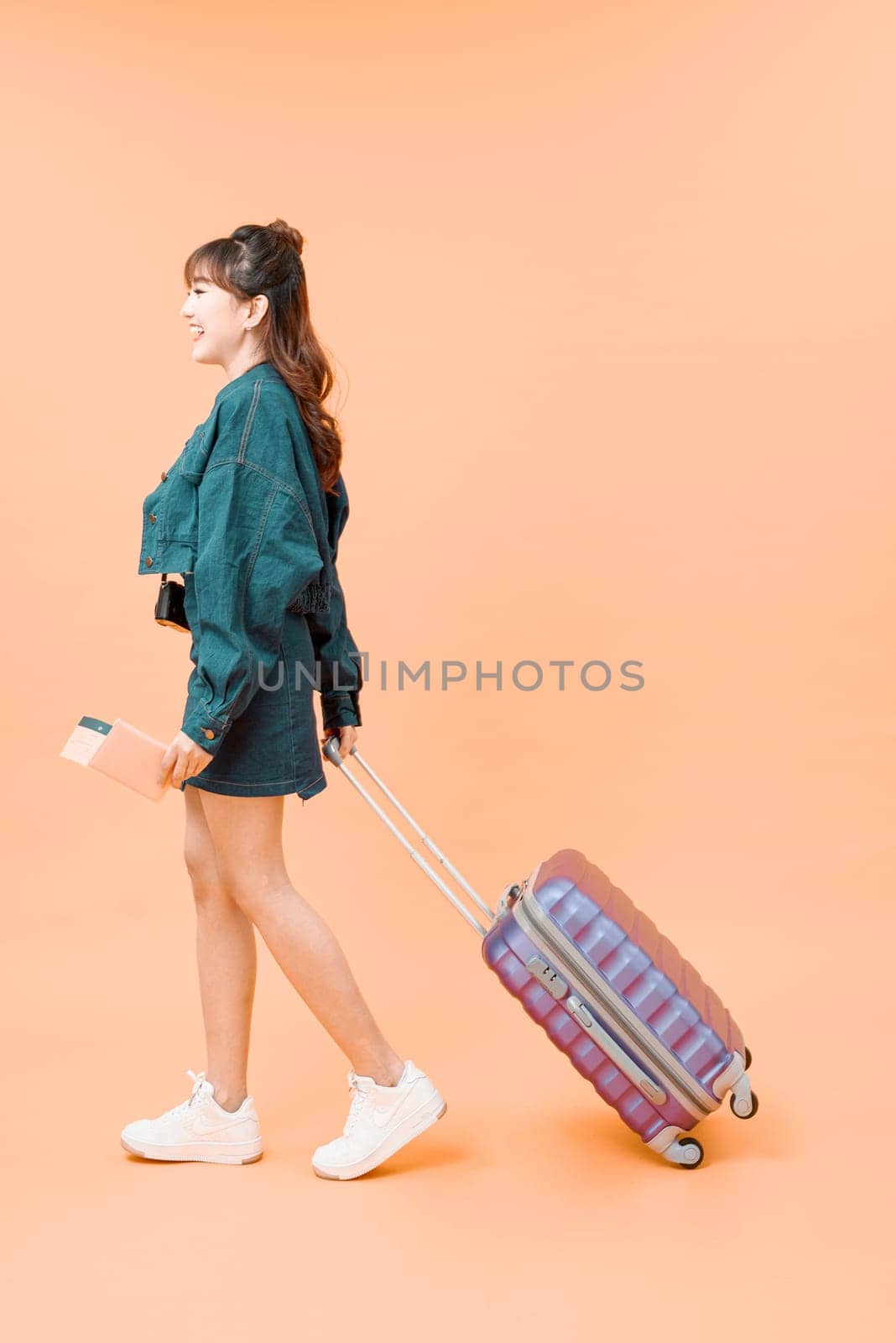 Travel concept. Full length studio portrait of pretty young woman holding passport with tickets walking with luggage