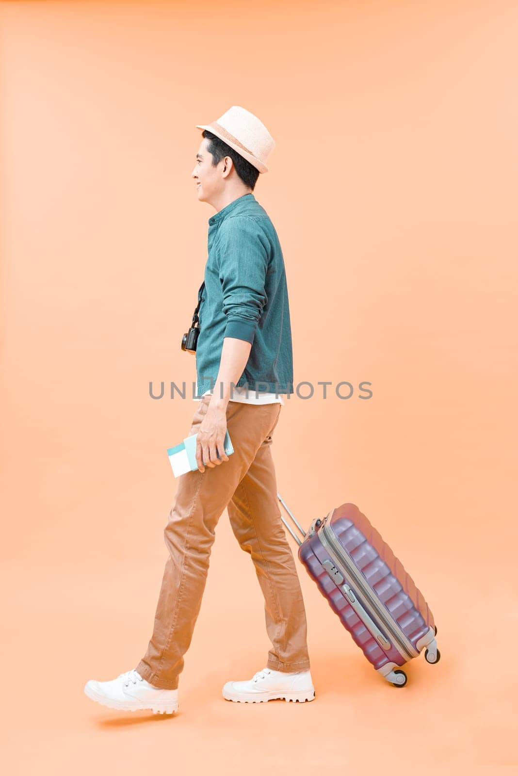 Full length of young asian man walking with the travel bag, isolated on color background
