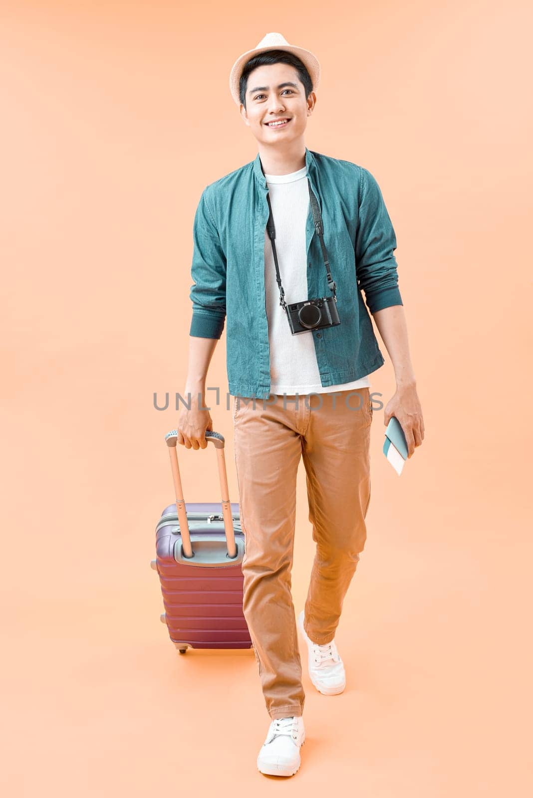 Happy asian male traveler walking with suitcase against color background by makidotvn