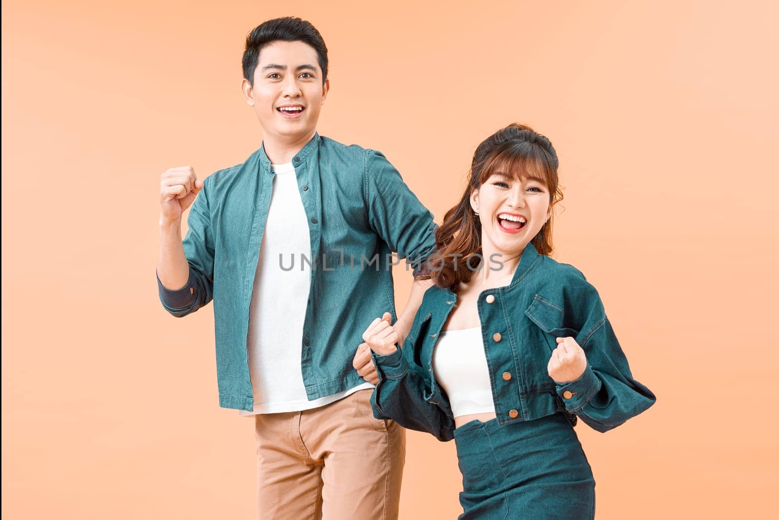 Portrait of an attractive cheerful young couple wearing casual clothing standing isolated over color background, celebrating success
