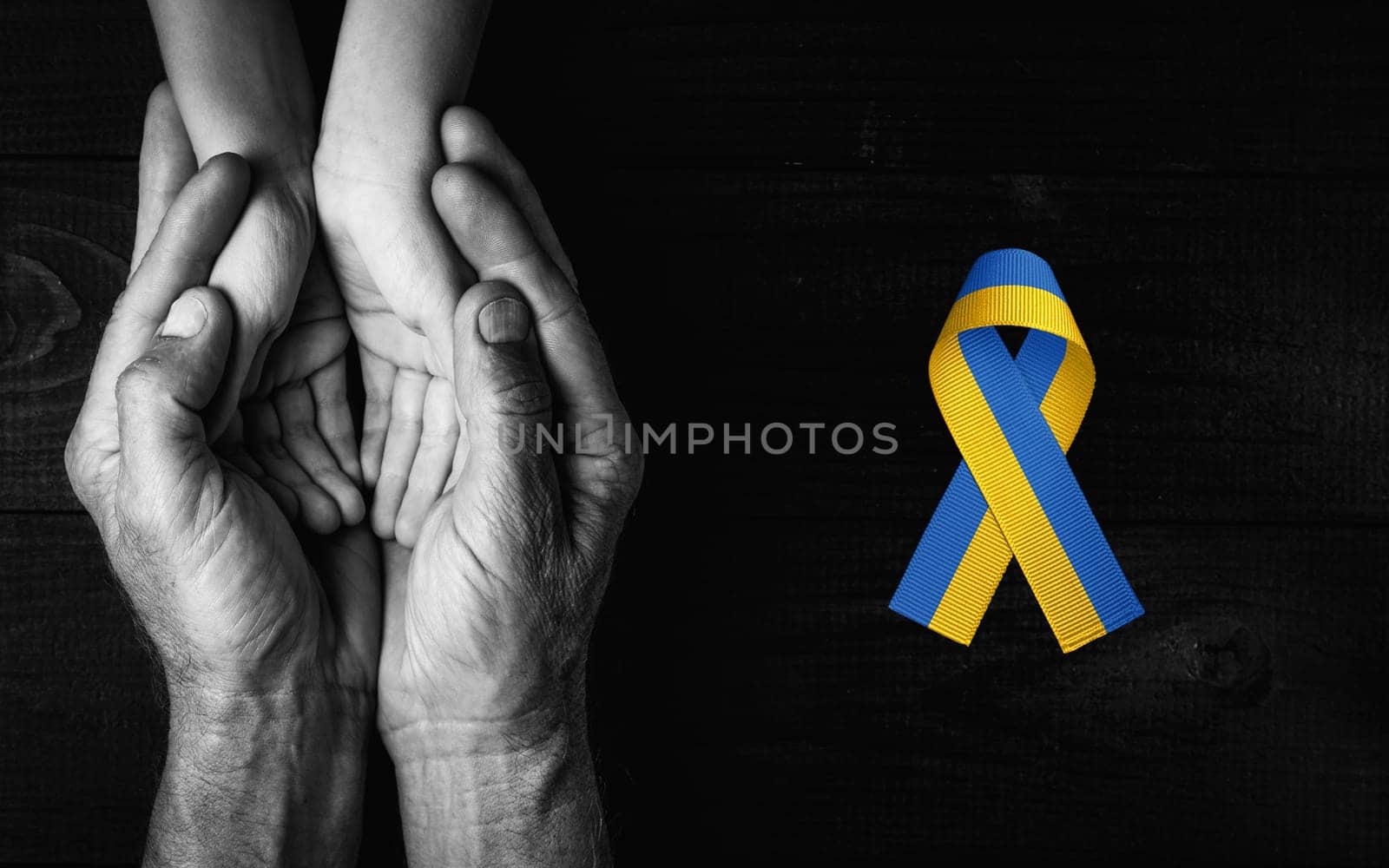 male hands hold childrens on dark wooden background with yellow and blue ribbon. black and white color. concept needs help and support, truth will win