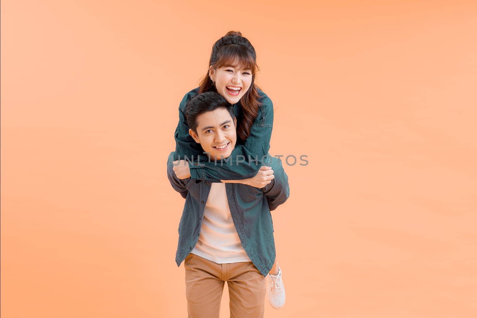 Handsome man giving piggy back to his girlfriend on color background